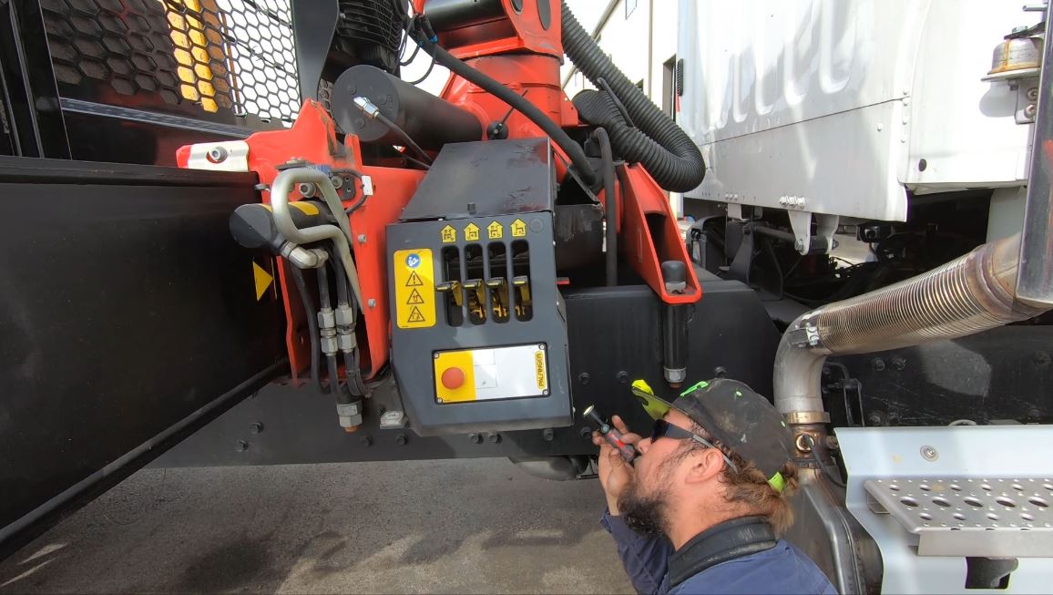 Nathan, holding a flashlight, inspecting the mounted operator's controls on a Palfinger crane